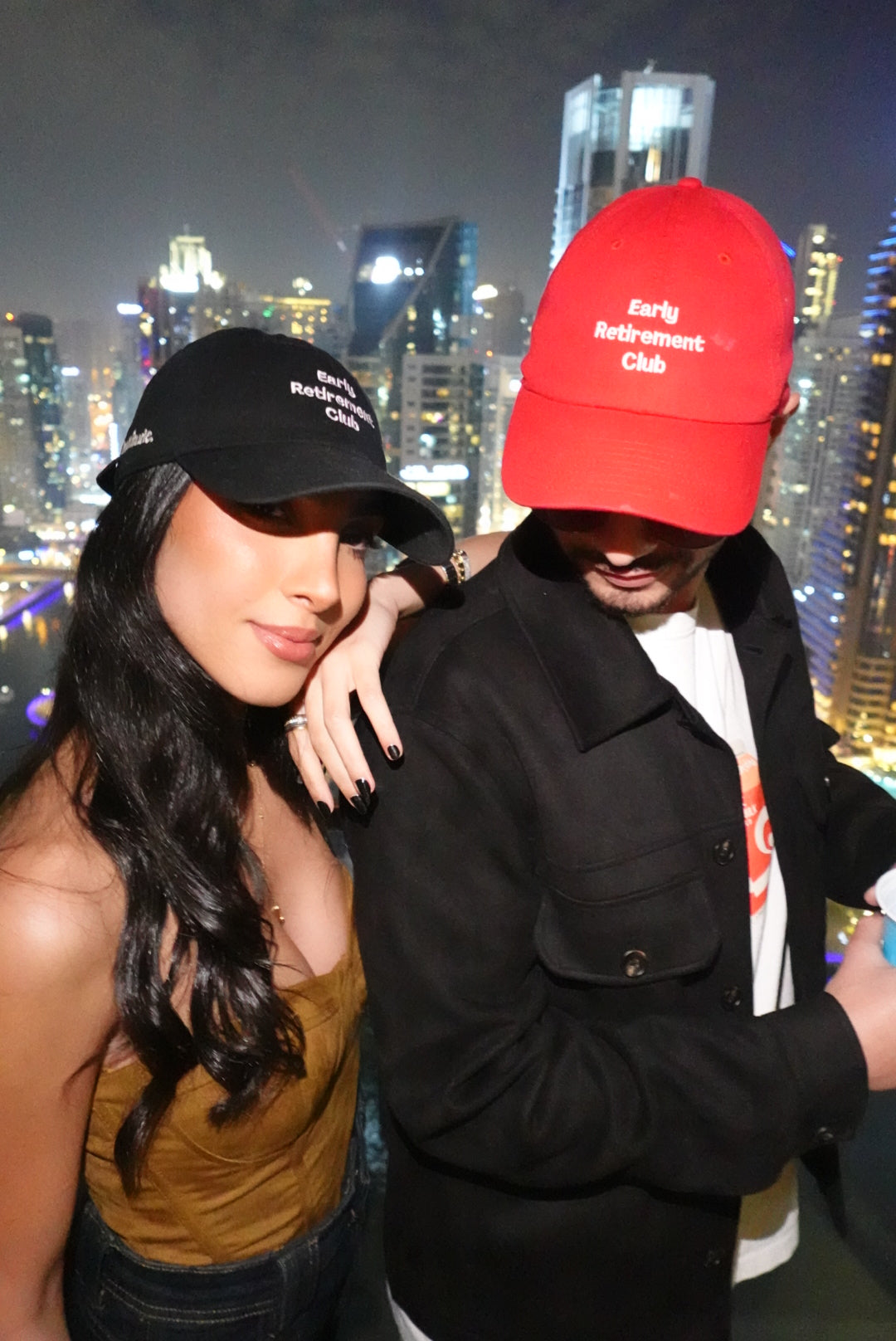 Two people wearing hattitude caps with a city skyline in the background
