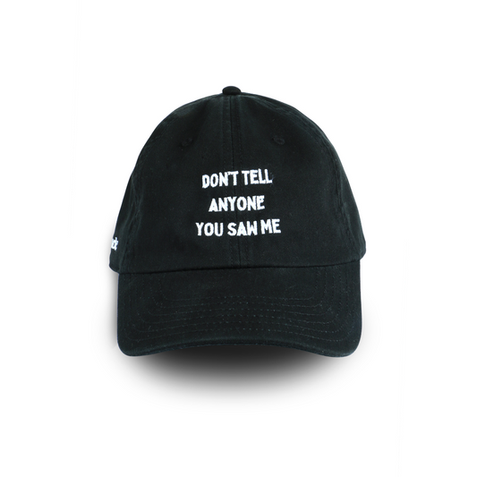 Black cap with subtle embroidered text “Don’t Tell Anyone You Saw Me,” sleek statement cap.