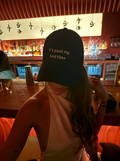 Person wearing a cap with text "it's past my bedtime" in a bar setting